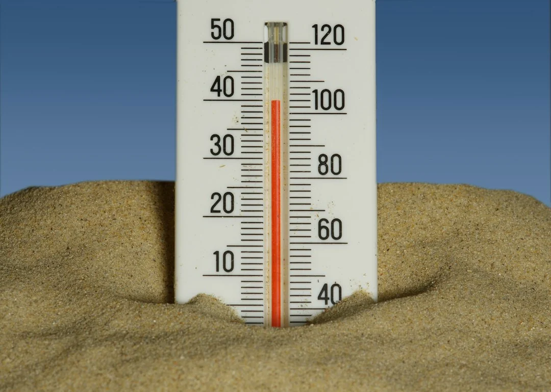 Outdoor thermometer with dual Celsius and Fahrenheit scales planted in sandy soil under a clear blue sky